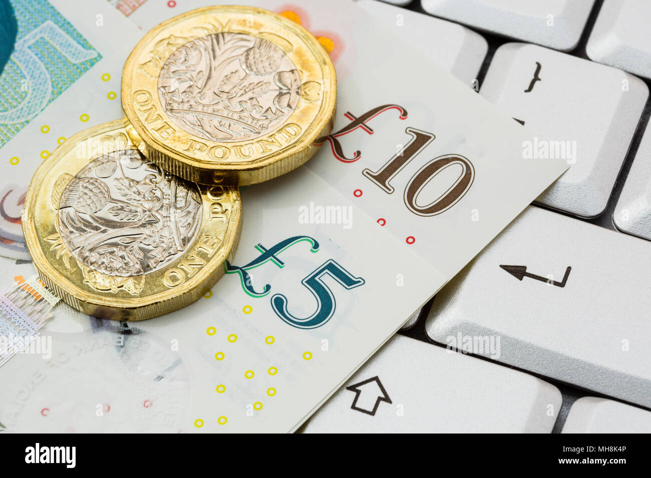 Sterling fünf und zehn Pfund Noten und 2 Neue Pfund-münzen Pfund Geld auf einem Keyboard mit ENTER-Taste. Online Investieren/Shopping Konzept. England Großbritannien Stockfoto