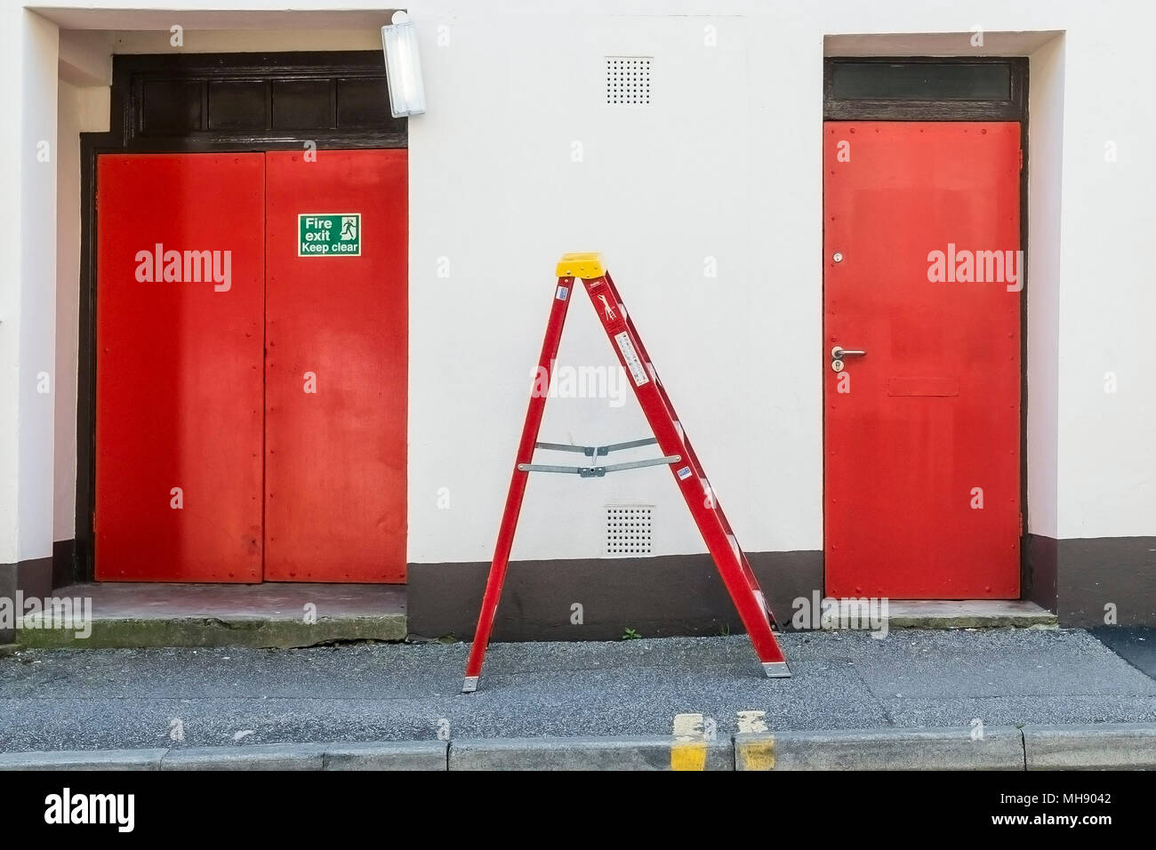 Ein roter Leiter zwischen zwei roten Türen. Stockfoto