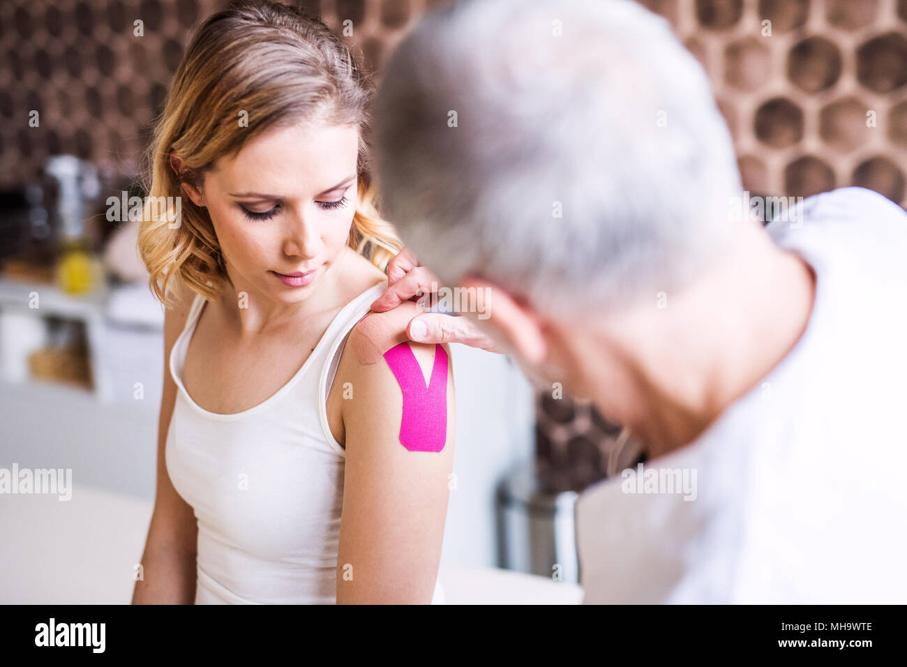 Ältere männliche Physiotherapeuten band Anwendung auf einem weiblichen Patienten. Stockfoto