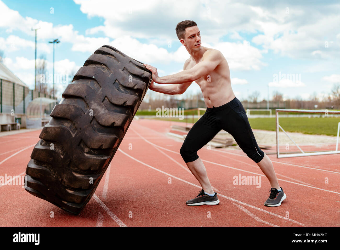 Junge muskulöse Mann oben schieben einen riesigen Reifen für Training Muskeln an der Tartanbahn auf dem Stadion. Stockfoto