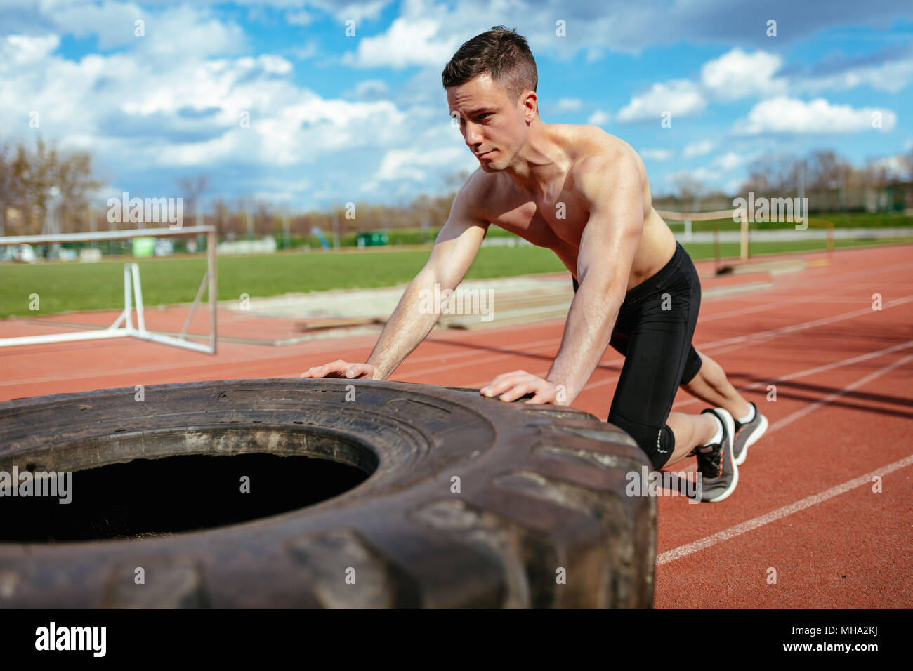 Junge muskulöse Mann oben schieben einen riesigen Reifen für Training Muskeln an der Tartanbahn auf dem Stadion. Stockfoto