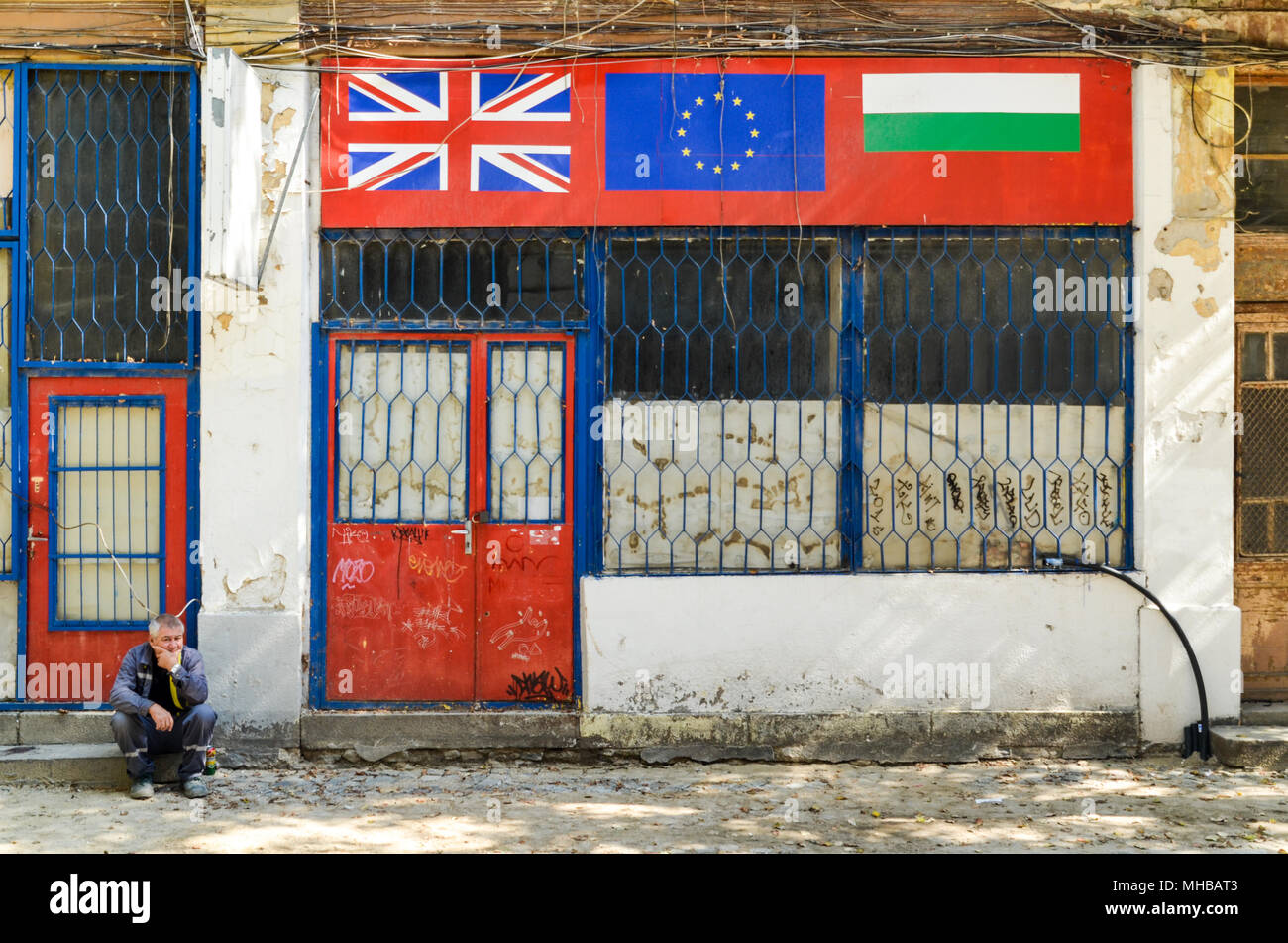 Alte Menschen sitzen, die durch eine Straße, vor einem Geschäft mit der Bulgarischen, UK und EU-Flaggen. Plovdiv, Bulgarien Stockfoto