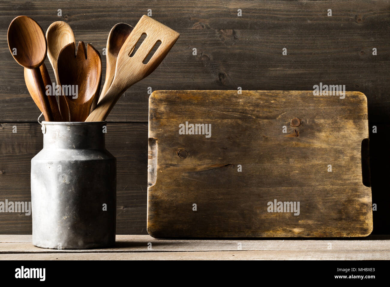 Küche kochen Werkzeuge mit Löffel und Spatel in Metall kann vor der rustikalen Holzbrett Hintergrund auf Holz Tisch mit leeren Menü board mit Stockfoto