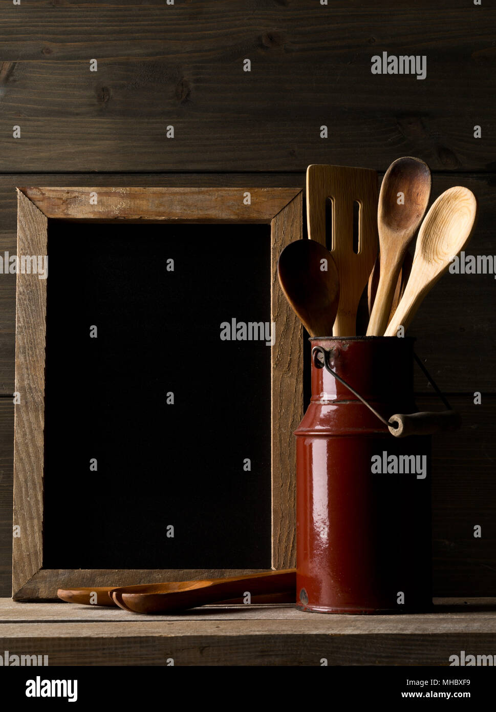 Küche kochen Werkzeuge mit Löffel und Spatel in Metall kann vor der rustikalen Holzbrett Hintergrund auf Holz Tisch mit leeren Menü board mit Stockfoto