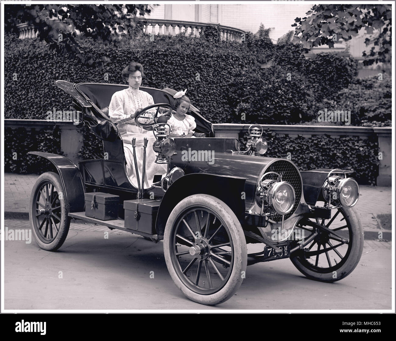 1907 Franklin Modell D Roadster. Frank Bliven war ein Washington, D.C. Franklin Auto Händler. Frau F.S. Bliven und Tochter sind vorhanden. Der Franklin Automobilunternehmen produzierten Fahrzeuge von 1902 bis 1934. Sie sind am besten für Luft erinnert - gekühlte Motoren, Holzrahmen und elliptisch Federn. Im Jahr 1907, das Modell D verfügbar war, als ein Vier-personen-Tourenwagen, in ein Runabout, oder einem 5-Person Landaulette. Das Modell D ruhte auf einem Radstand, 105-Zoll gemessen und durch eine 4-Zylinder Motor, 20 PS der Großen Depression für eine Beendigung der Marke verantwortlich war Angeboten versorgt. Stockfoto