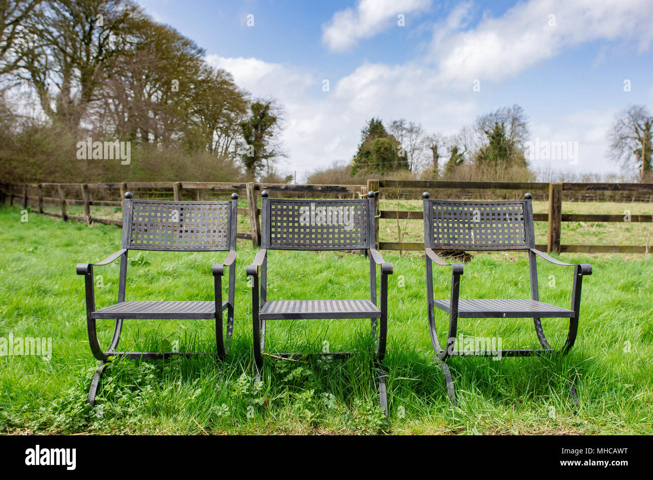 Drei antike Bügeleisen terrasse Stühle in der ungeschnittenen Grases stehend Stockfoto