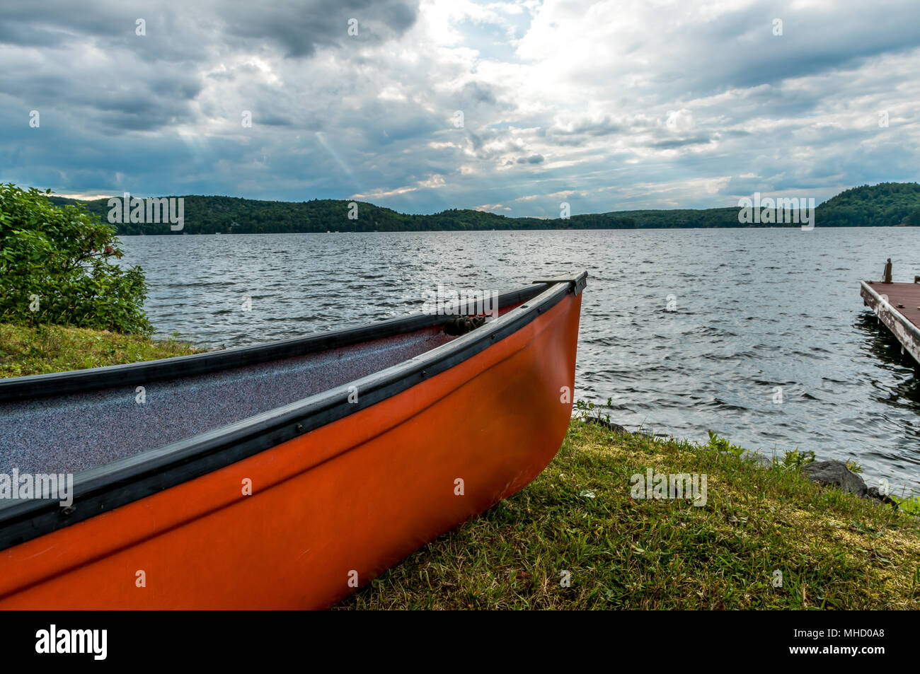 Rote Kanu auf dem Ufer, mit dramatischen Sonnenlicht am Abend bewölkten Himmel. Stockfoto