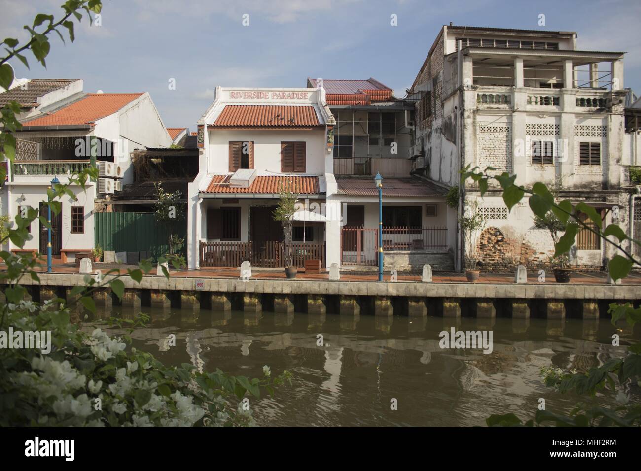 Eine Terrasse von Häuser säumen den Fluss in Malakka, Malaysia. Ruhiges Wasser spiegelt verzerrte Bilder der Häuser über. Stockfoto