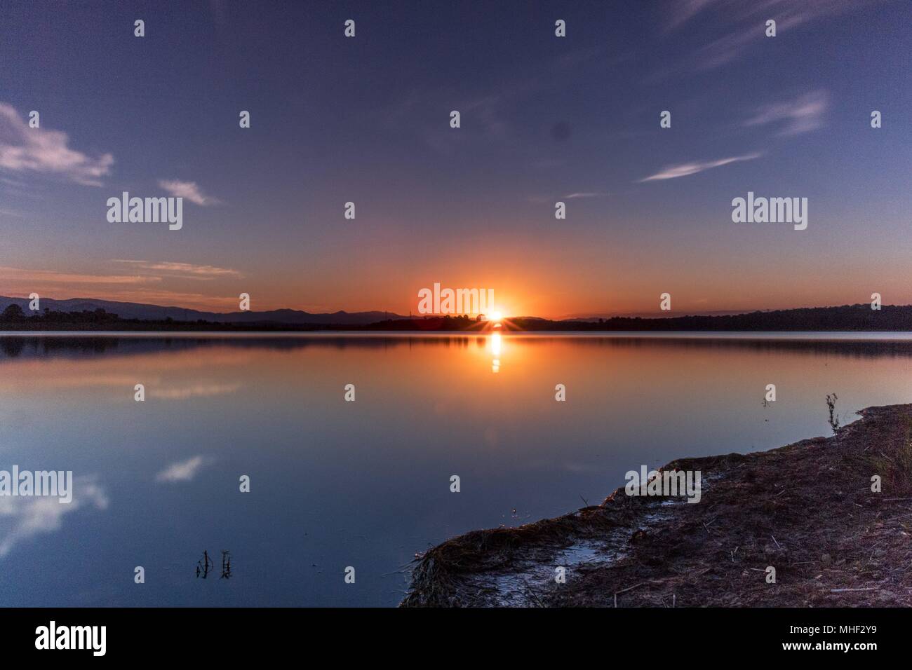 Die Bilder zeigen ein Sonnenuntergang über einem ruhigen See genau im richtigen Moment wie der reflektierten Sonnenstrahlen, den Himmel, während die Symmetrie mit dem Wasser Licht. Stockfoto