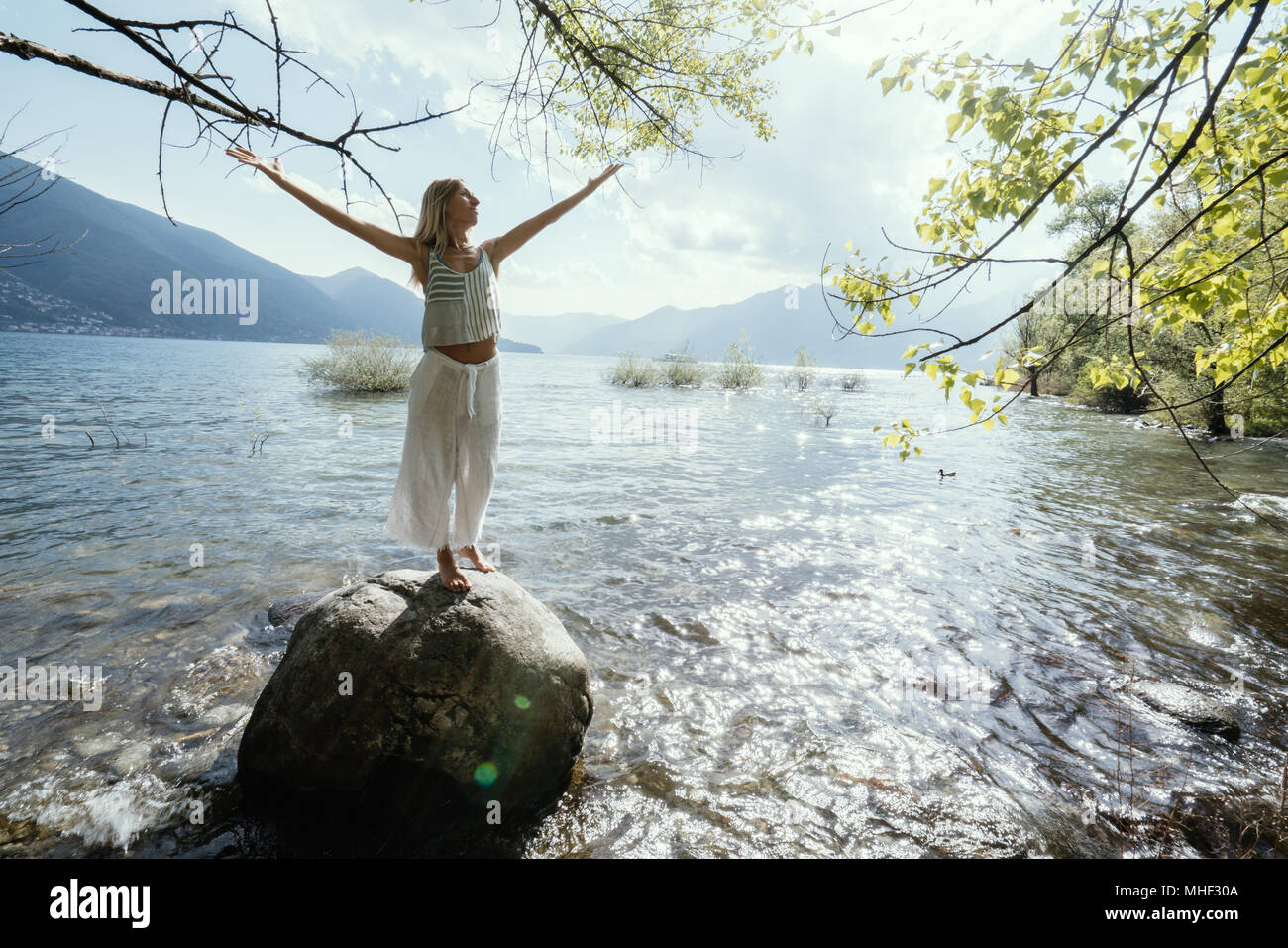 Junge Frau, die auf den Felsen über dem See Waffen für Freiheit und positive Emotionen ausgestreckt. Die Menschen reisen Wohlbefinden sorglos Konzept. Schweiz Stockfoto