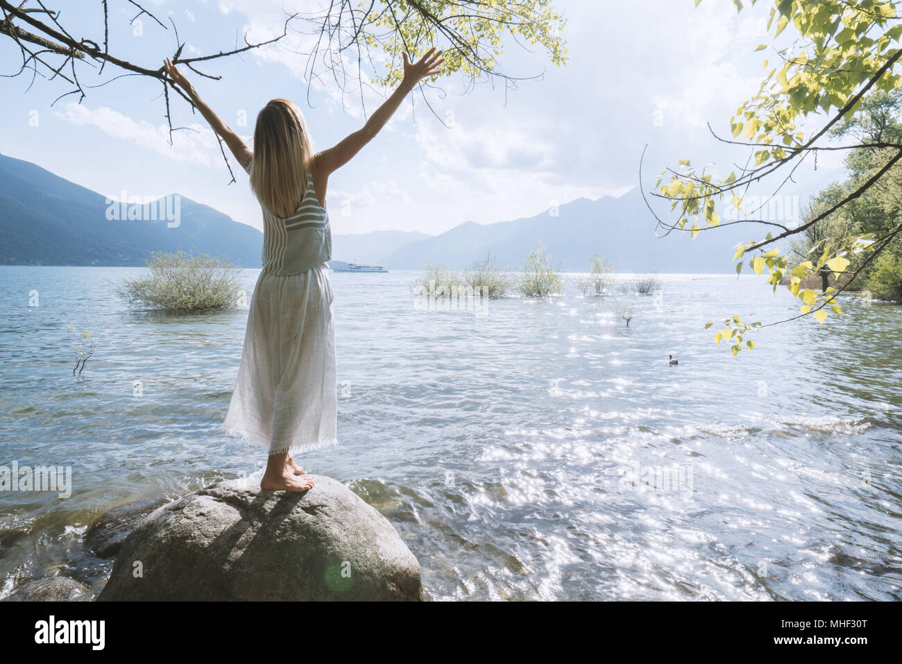 Junge Frau, die auf den Felsen über dem See Waffen für Freiheit und positive Emotionen ausgestreckt. Die Menschen reisen Wohlbefinden sorglos Konzept. Schweiz Stockfoto
