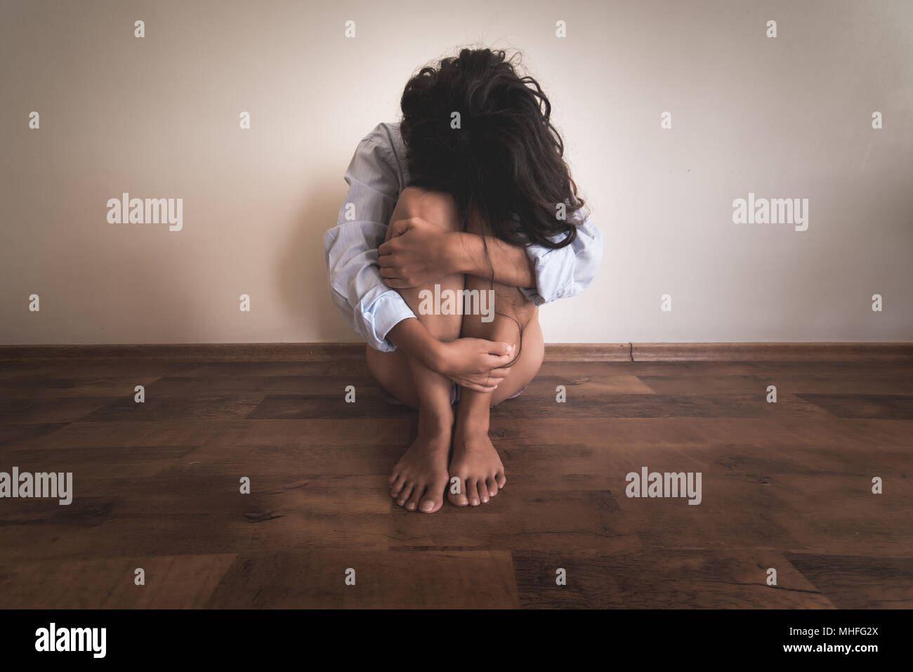 Eine traurige Frau sitzt auf dem Boden in der Nähe einer Wand und Ihre Beine halten in ihren Händen Stockfoto