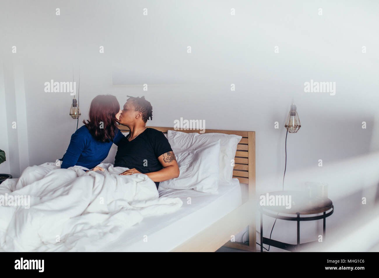 Romantisches Paar Küssen im Bett. Interracial Mann und Frau sitzt auf dem Bett und küssen sich. Stockfoto