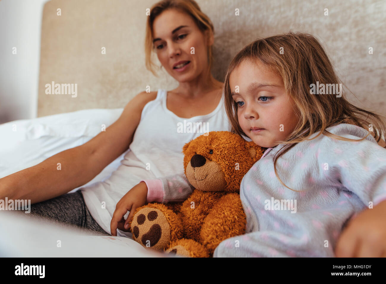 Kleine Mädchen lesen ein Interesse Buch sitzen auf dem Bett mit ihrer Mutter. Mutter und Tochter ein Buch lesen im Bett. Stockfoto