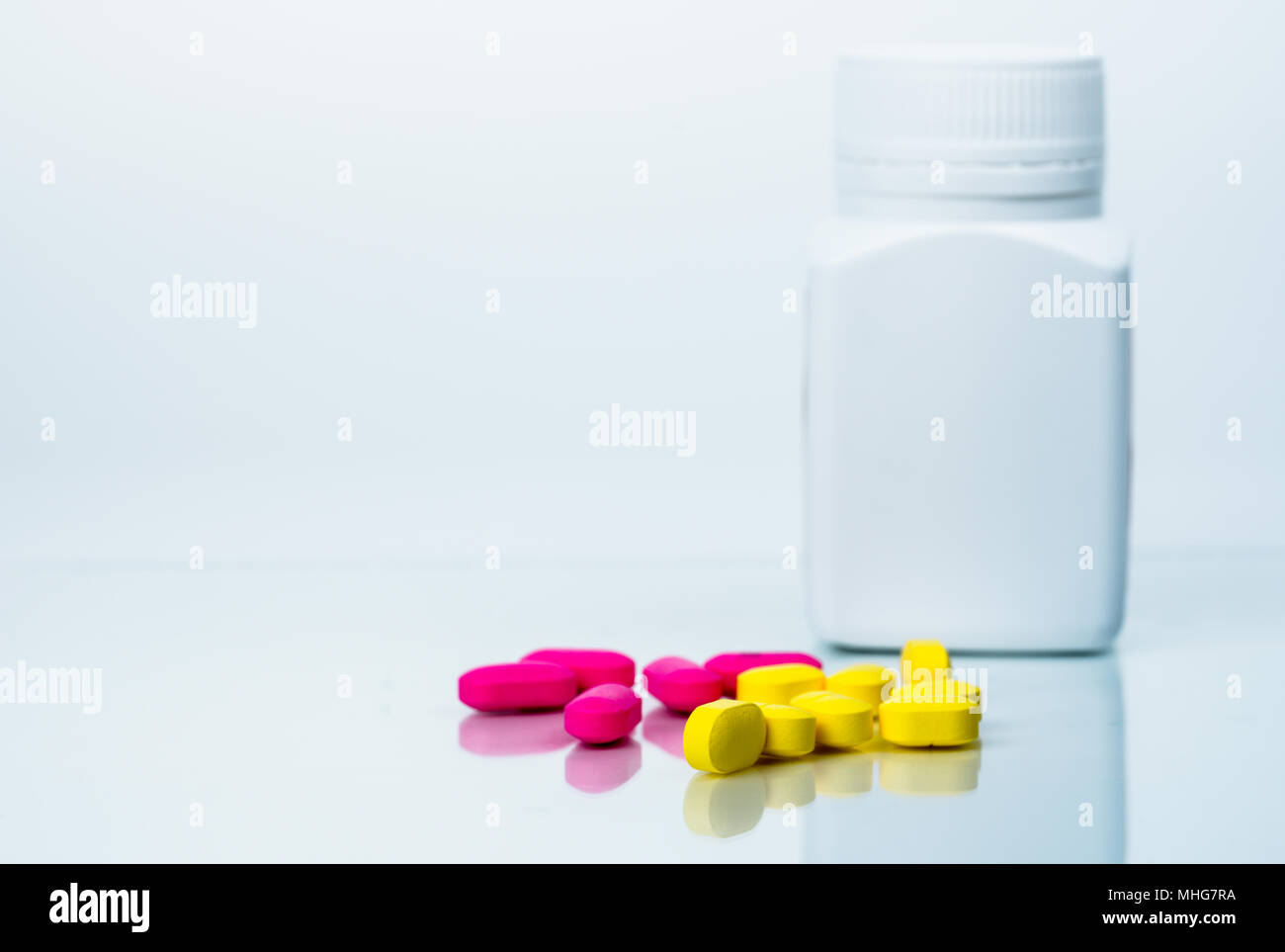 Stapel von rosa und gelbe Tabletten Pillen in der Nähe von Kunststoff pillen Flasche mit leeren Label auf weißem Hintergrund mit Kopie Raum isoliert. Ibuprofen für Entlastung pa Stockfoto