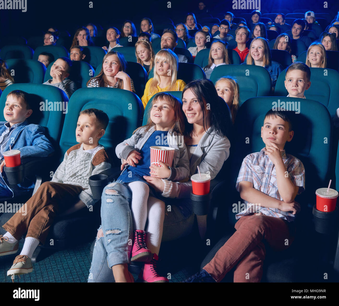Kinder, Jugendliche, Erwachsene, Film mit unerschütterlichem Augen im modernen Kino. Lächelnd Zuschauer Snacks essen, sitzen in bequemen Stühlen. Konzept der Kinematographie und Unterhaltung. Stockfoto