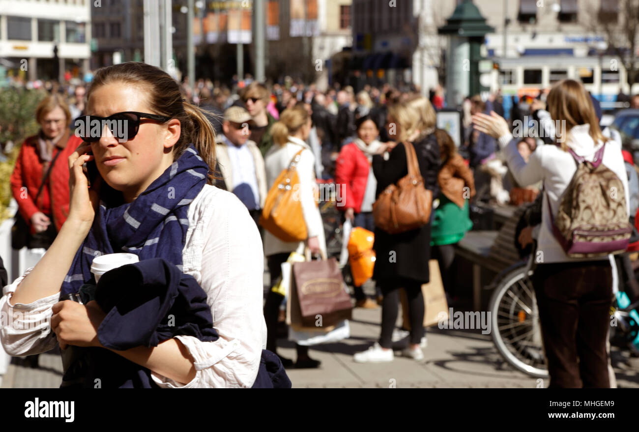 Göteborg - 20. April 2013: eine Frau mit Sonnenbrille im Vordergrund telefonieren in der frühlingssonne an thes quare Kungstorget mit Menschen flanieren Stockfoto