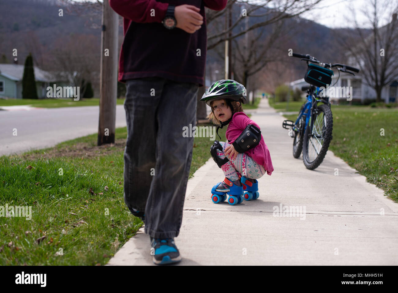 Eine Schwester und Bruder draußen spielen auf einem Bürgersteig mit einem Fahrrad und Skates. Stockfoto