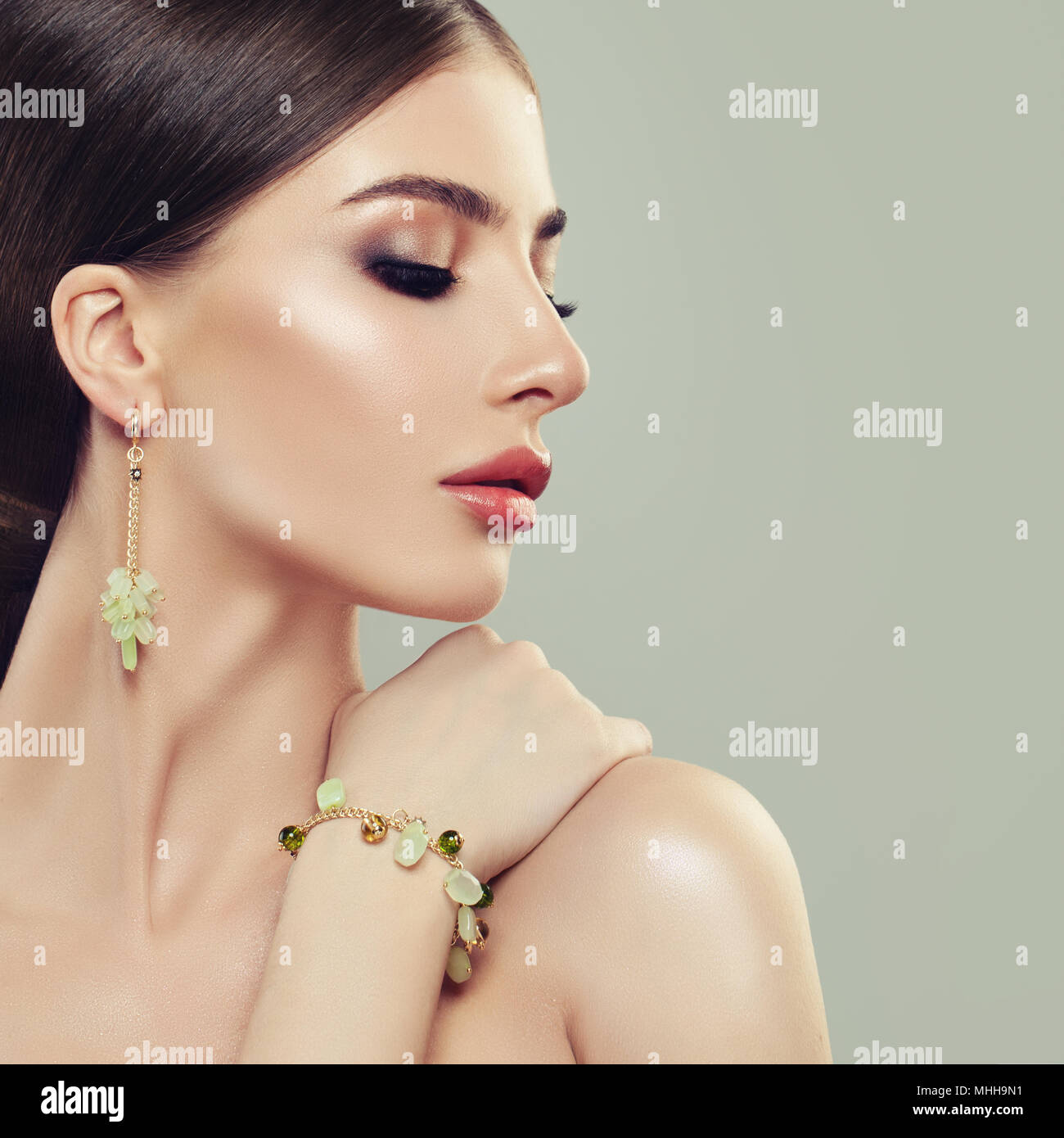 Schönen weiblichen Gesichts Closeup Portrait. Perfekte Frau mit Make-up und Schmuck Gold Armband und Ohrringe mit grünen Edelstein Stockfoto