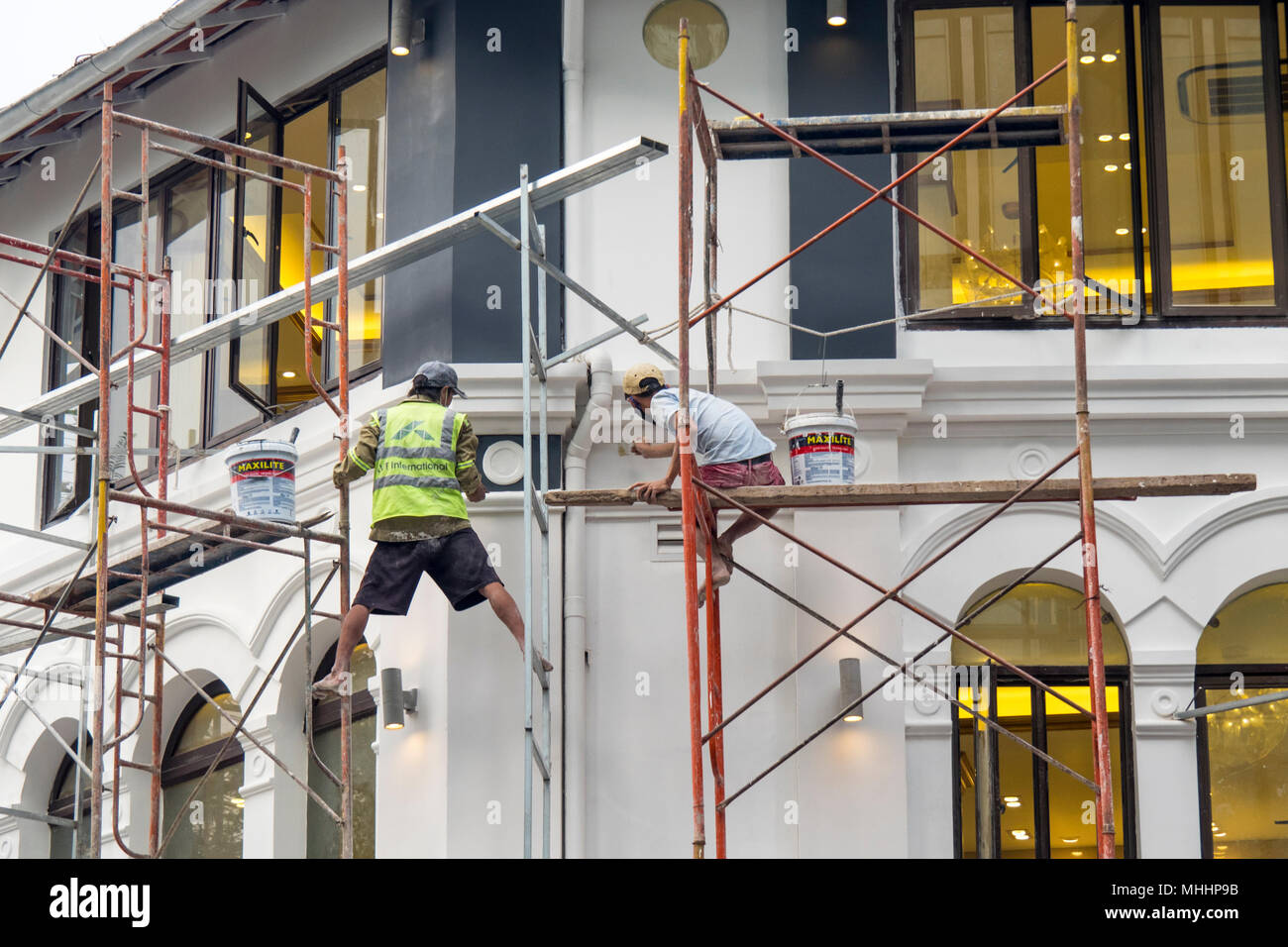 Zwei Männer auf einem Gerüst arbeiten unter unsicheren Bedingungen Malerei Französischen Kolonialstil Gebäude im District 1, Ho Chi Minh City, Vietnam. Stockfoto