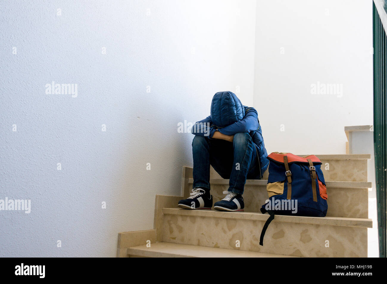 Traurige Junge mit Rucksack allein in der Ecke im Treppenhaus Stockfoto
