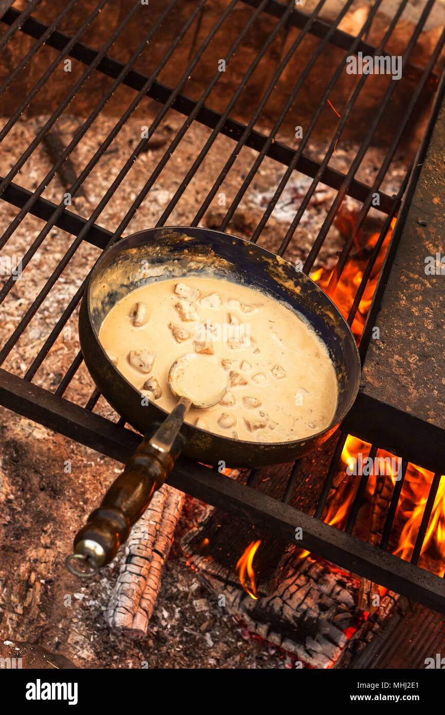 Emaillierte Pfanne auf Feuer. Vorbereitung des Pilzes Steak Sauce. Feuer im Lager Stockfoto