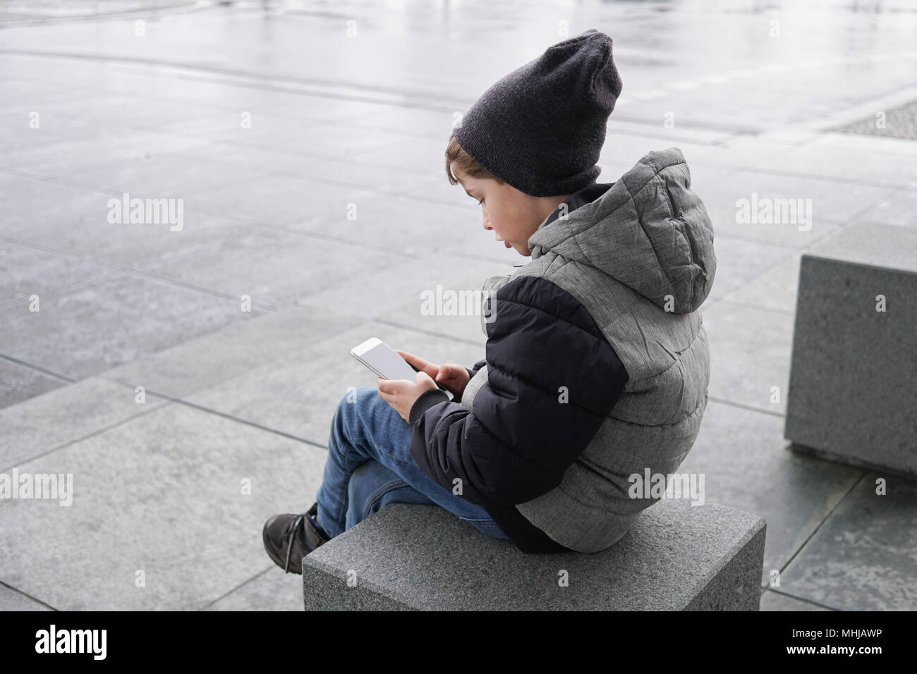 Candid Foto von Jungen mit Smartphone Handy draußen sitzen allein auf der Straße im Winter Stockfoto