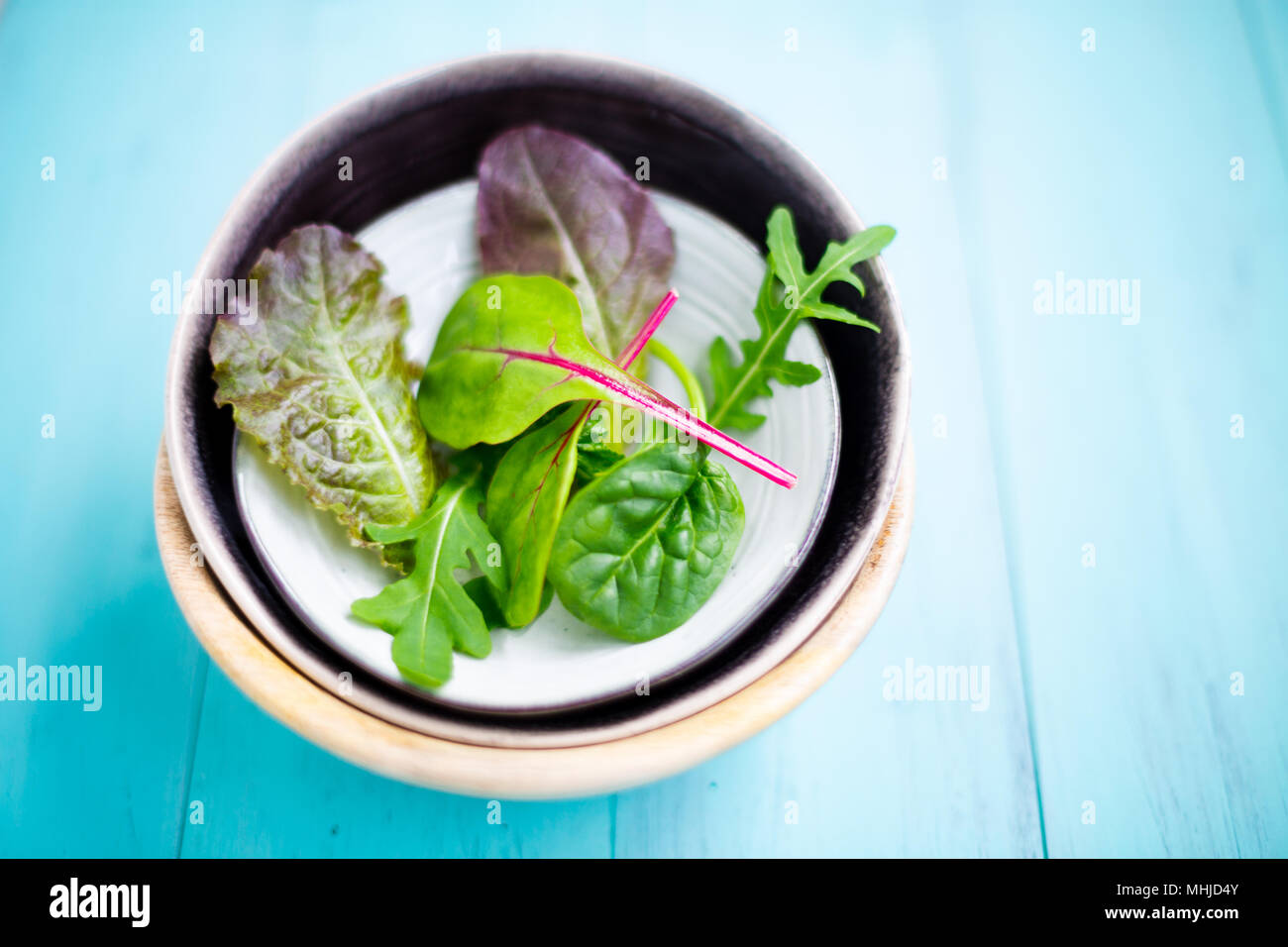 Gemischter Salat von Baby leaf red Chard, Rucola, rote Kopfsalat und tatsoi in kleinen Schalen auf einem aquamarin Holztisch, selektiver Fokus Stockfoto