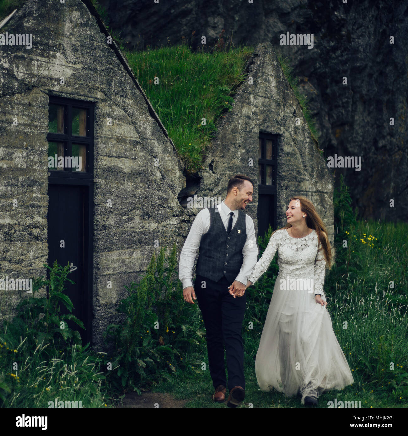 Junge stilvolle Mode Paar in Liebe in Island. Frau und Mann umarmen und möchten einander zu küssen. Stein Berge und isländischer Haus im Hintergrund. Stockfoto