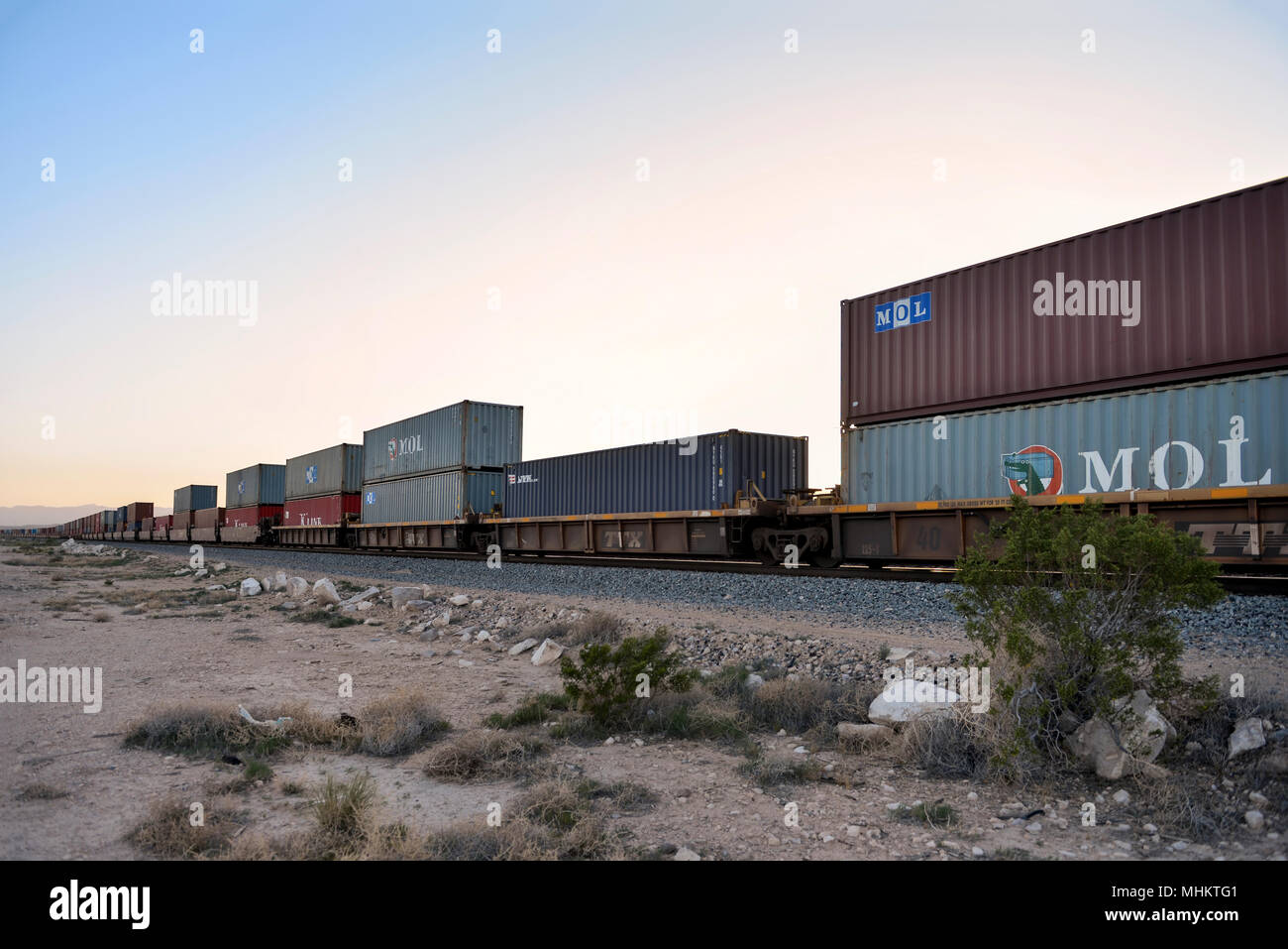 Cargo Container mit dem Zug durch die Wüste von Nevada in der Dämmerung unterwegs. Stockfoto