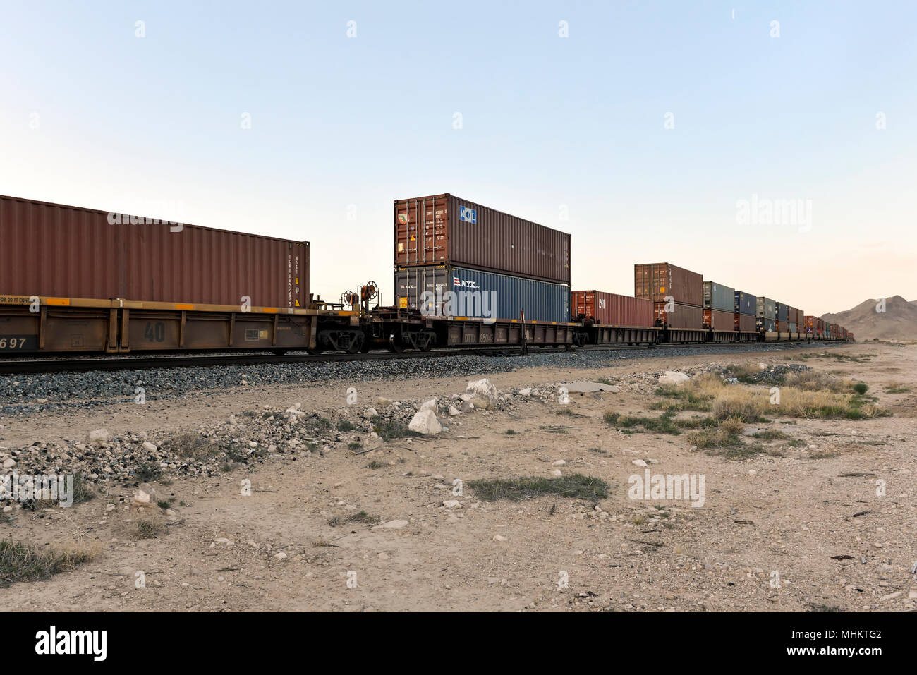Cargo Container mit dem Zug durch die Wüste von Nevada in der Dämmerung unterwegs. Stockfoto