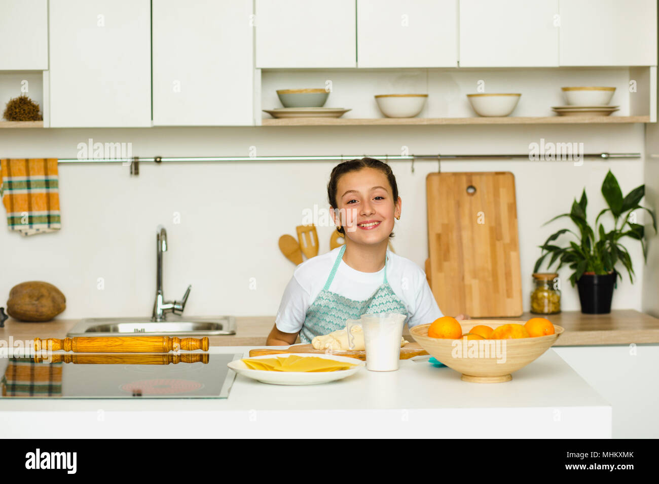 Schöne Mädchen in eine Schürze gekleidet, die Vorbereitung von orange Kuchen, in einem wunderschönen Haus Küche stehen. Glückliches Kind ist Kochen Stockfoto