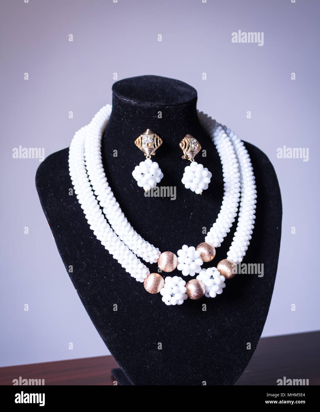 Handgefertigte Kette aus weißen und goldenen Perlen mit passenden Ohrringen auf einem schwarzen Mannequin Stockfoto