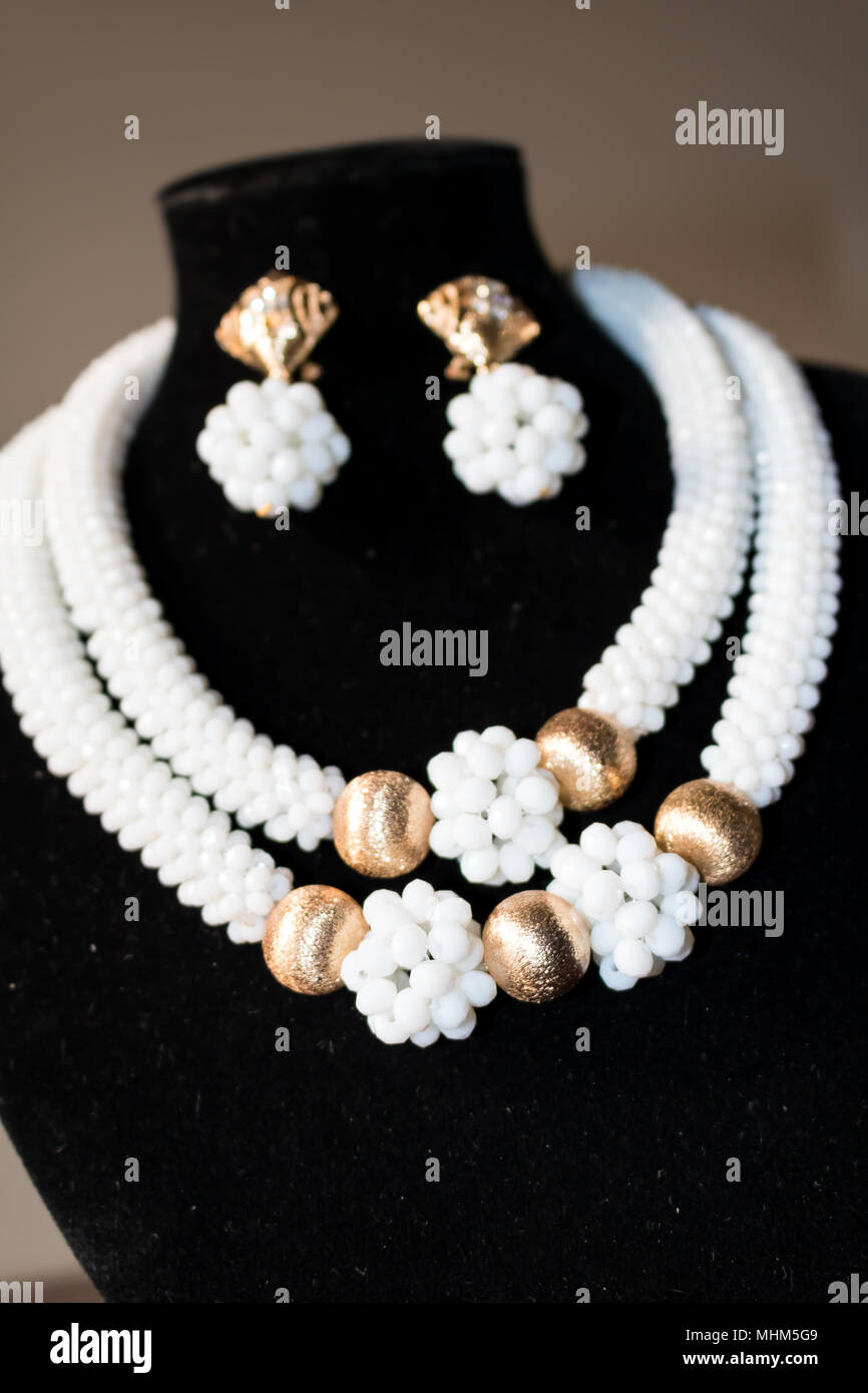 Handgefertigte Kette aus weißen und goldenen Perlen mit passenden Ohrringen auf einem schwarzen Mannequin Stockfoto