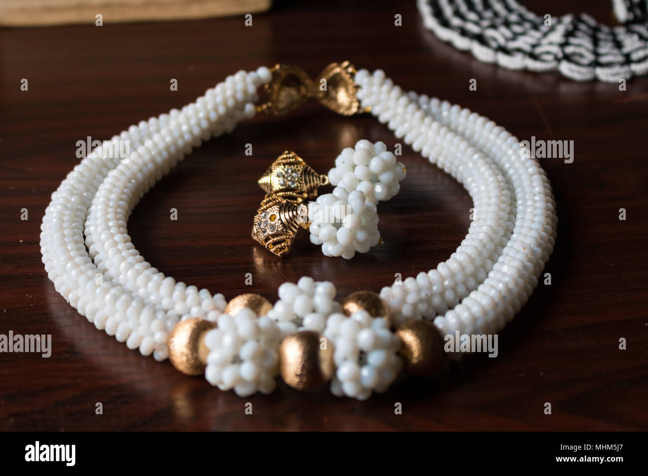 Handgefertigte Kette aus weißen und goldenen Perlen mit passenden Ohrringen und goldener Schnalle auf einem braunen Tisch Stockfoto