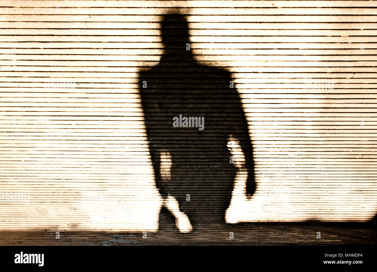 Verschwommene Schatten Silhouette eines Mannes zu Fuß auf gemusterten Bürgersteig Stockfoto