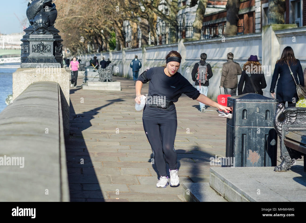Plogging UK. Frau Joggen entlang der Southbank durch den Fluss in London, herauf und Wegwerfen von Müll in einem Abfallbehälter. Stockfoto