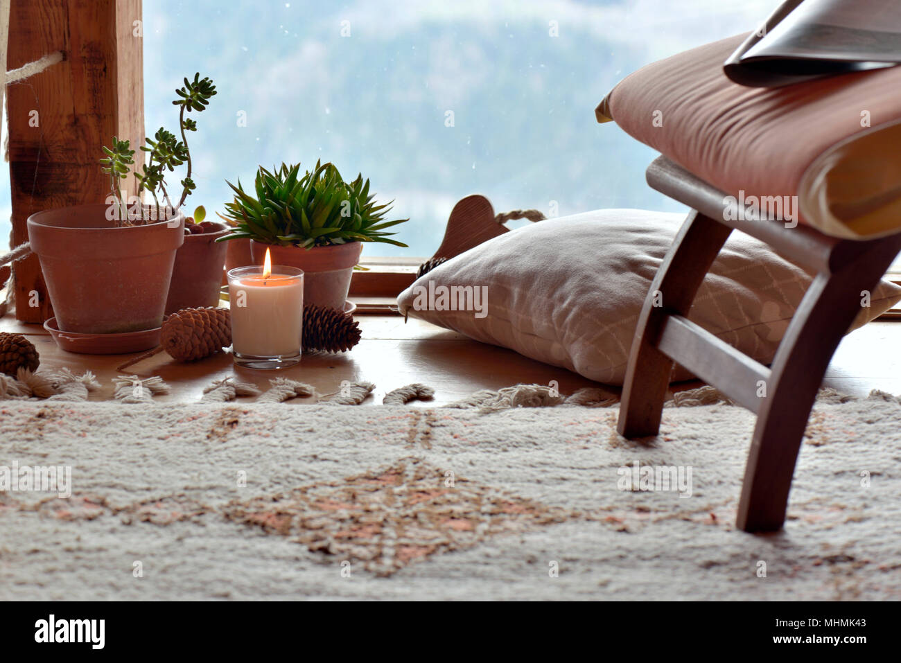 Pausenraum mit Stuhl, Pflanzen und Kerze vor paned Glas in einer Hütte in den Bergen Stockfoto