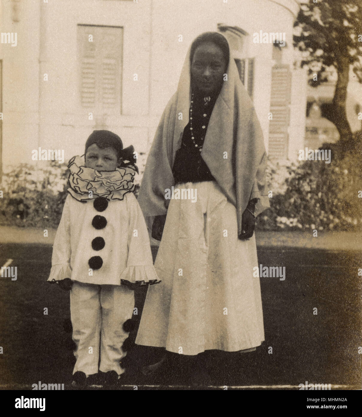 Ein kleiner Junge, gekleidet in einen Clown Kostüm für eine Party. Er scheint durch seine Krankenschwester oder Ayah - das Foto sieht auf dem indischen Sub - Kontinent ergriffen werden begleitet werden. Datum: 1920 s Stockfoto