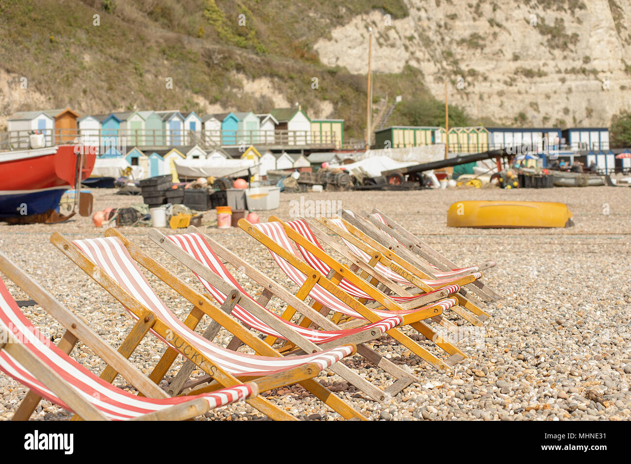 Eine Reihe von leeren traditionellen hölzernen Rahmen, Liegestühle mit rot-weiß gestreifte Material auf einem Kieselstrand mit Umkleidekabinen und Kreidefelsen auf der Rückseite Stockfoto