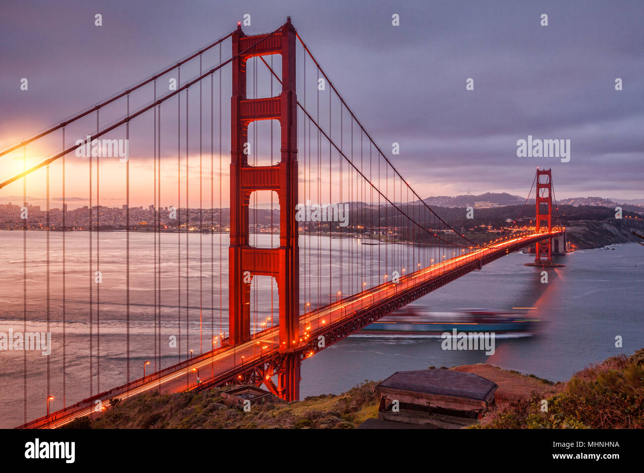 Die Golden Gate Bridge, San Francisco, von der Batterie Spencer in der Dämmerung, mit Verkehr auf der Brücke und einem Container schiff aus dem Schacht heraus. Stockfoto