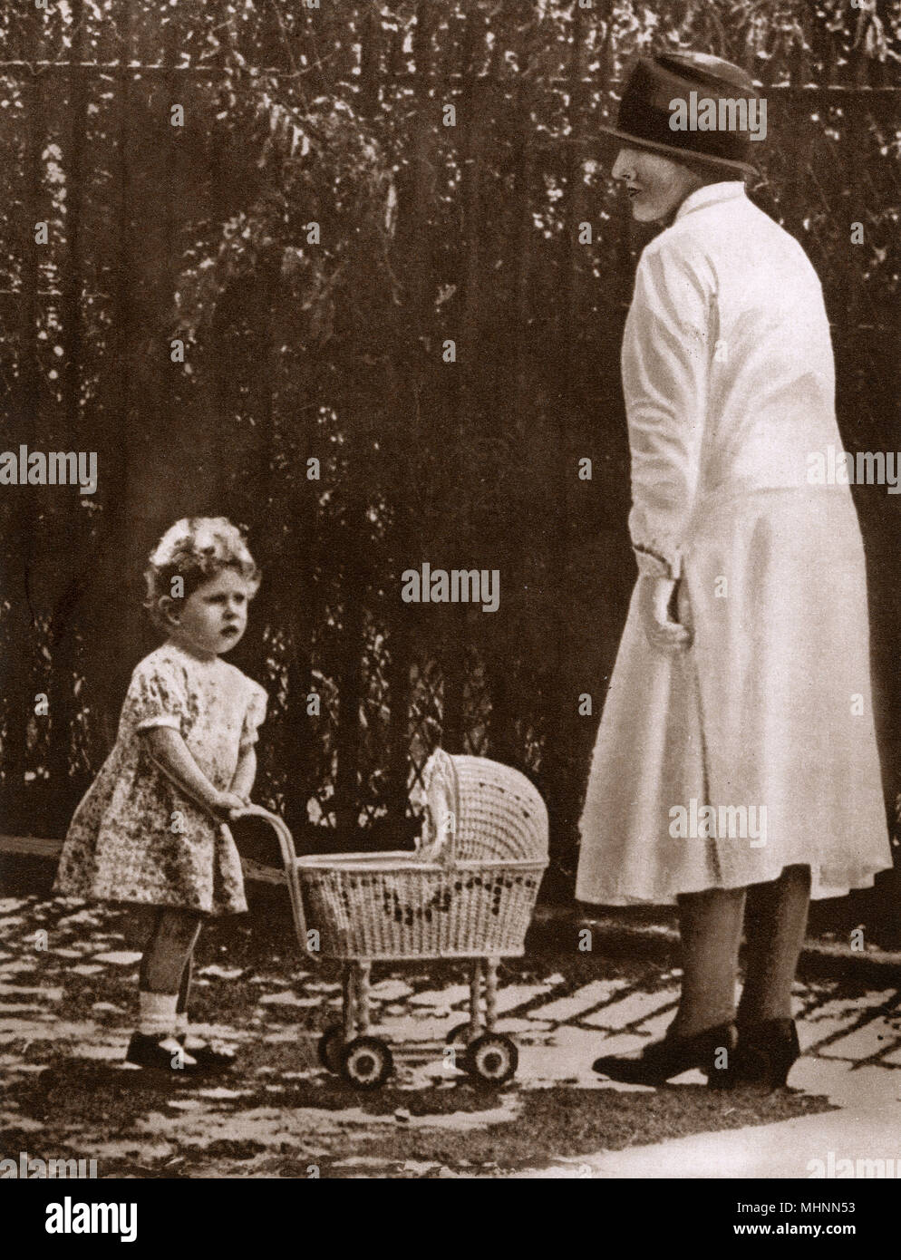 Junge Prinzessin Elizabeth (später Königin Elizabeth II) (1926-) mit ihrem ersten Spielzeug Kinderwagen auf dem Grundstück ihrer Eltern zu Hause in Piccadilly mit ihrem Kindermädchen. Datum: 1928 Stockfoto