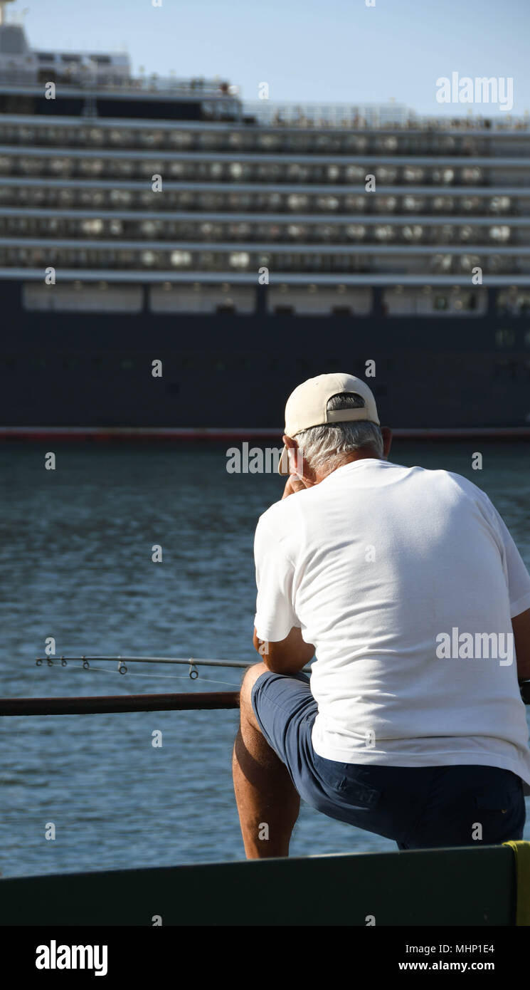 Person angeln von der Hafenseite in Funchal, Madeira. Das kreuzfahrtschiff Queen Elizabeth ist im Hintergrund Stockfoto