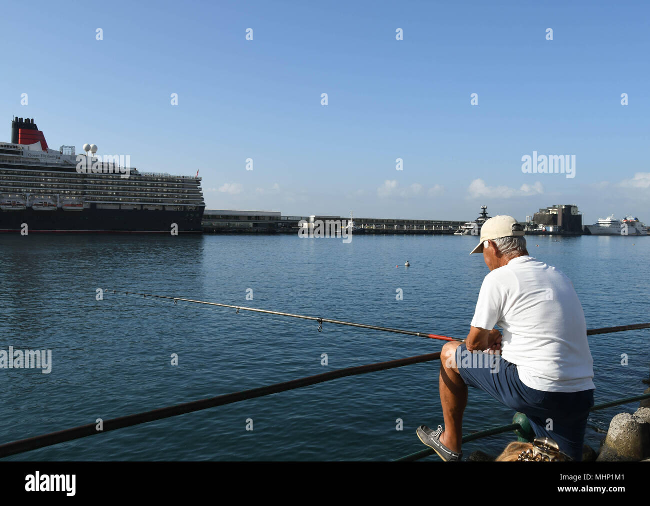 Person angeln von der Hafenseite in Funchal, Madeira. Das kreuzfahrtschiff Queen Elizabeth ist im Hintergrund Stockfoto