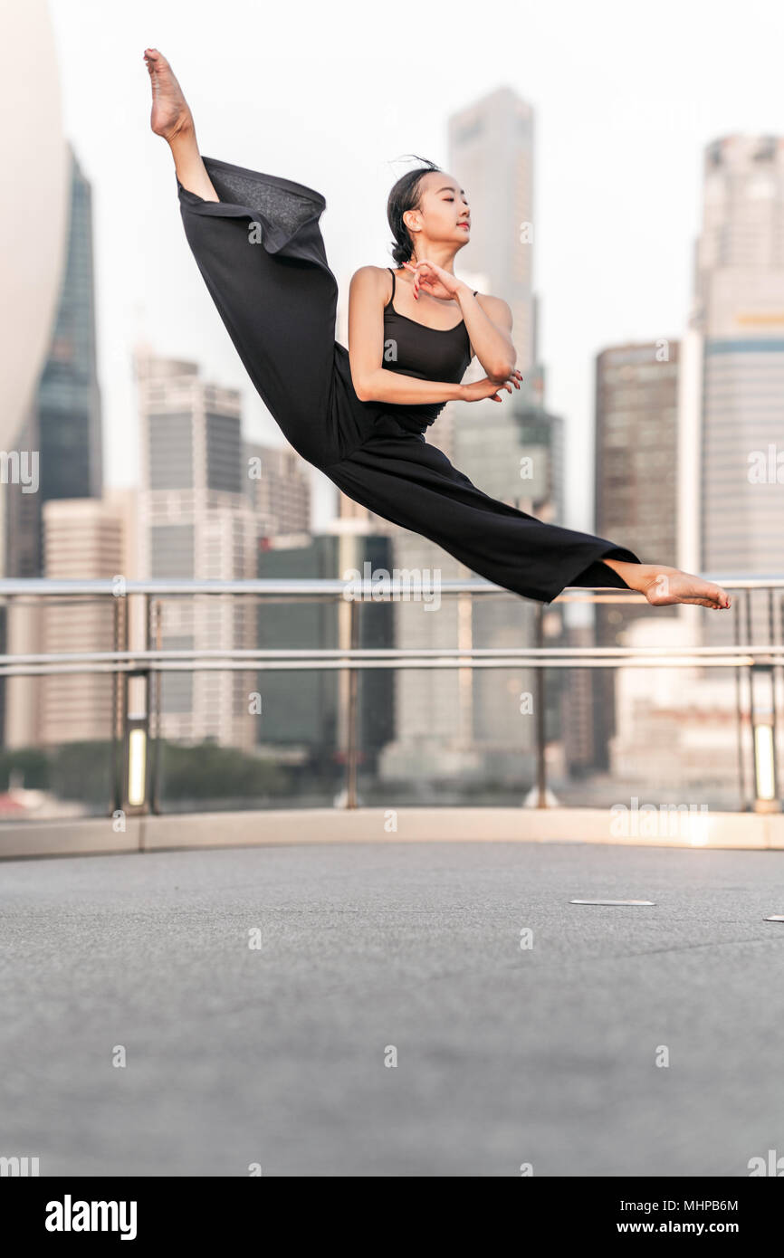 Nette junge Sportlerin führt einen perfekten Sprung hoch oben, auf einer Brücke mit Hintergrund der Wolkenkratzer Stockfoto