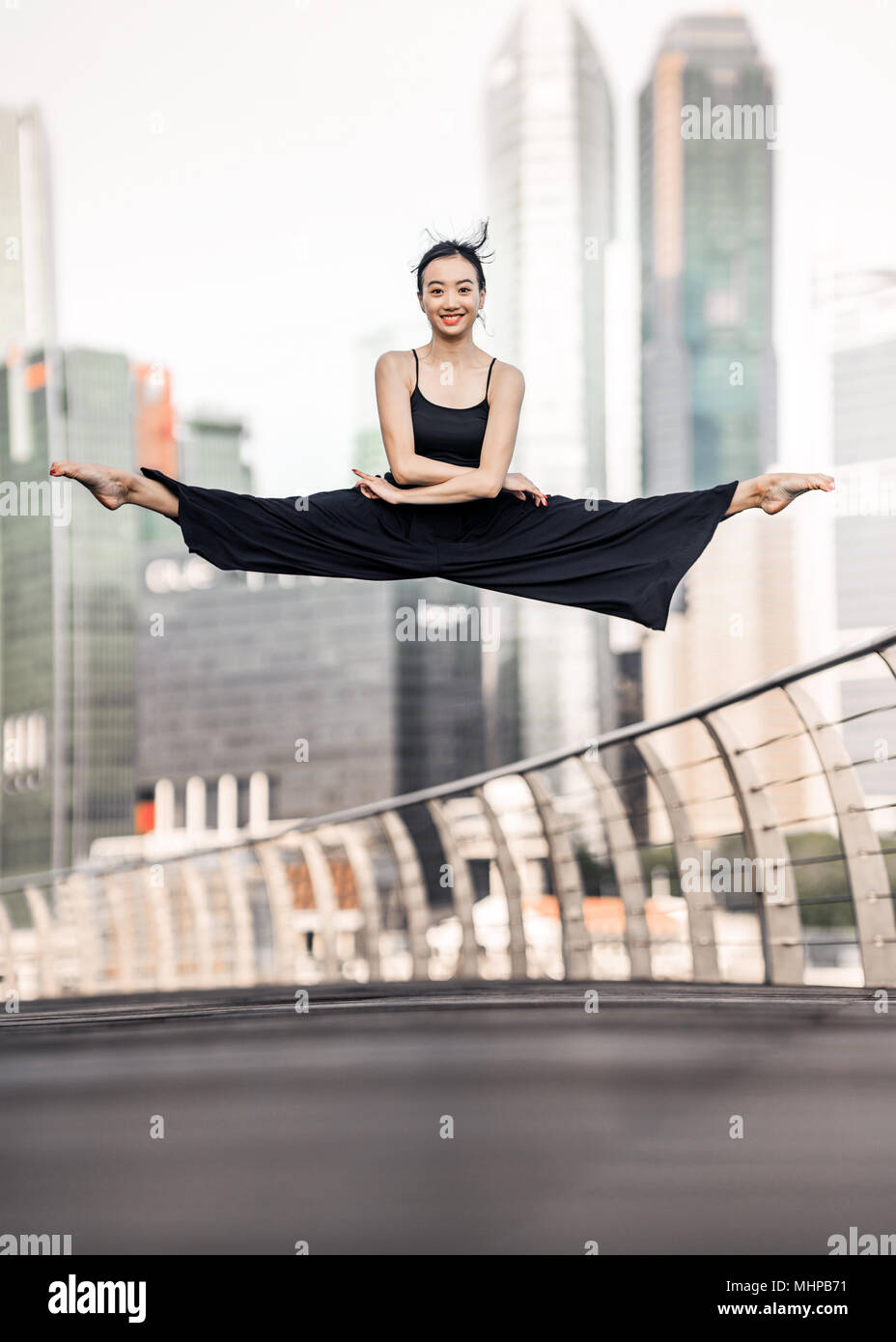 Nette junge Sportlerin mit schönen Lächeln führt eine perfekte straddle Sprung hoch oben, auf einer Brücke mit Hintergrund der Wolkenkratzer Stockfoto