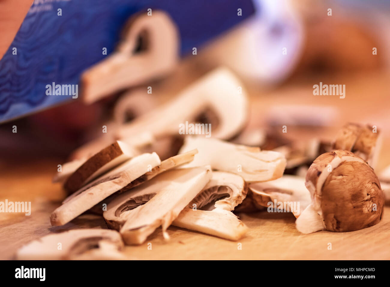 In Scheiben geschnittenen Champignons auf Holz Schneidebrett, blau Messerklinge. Stockfoto