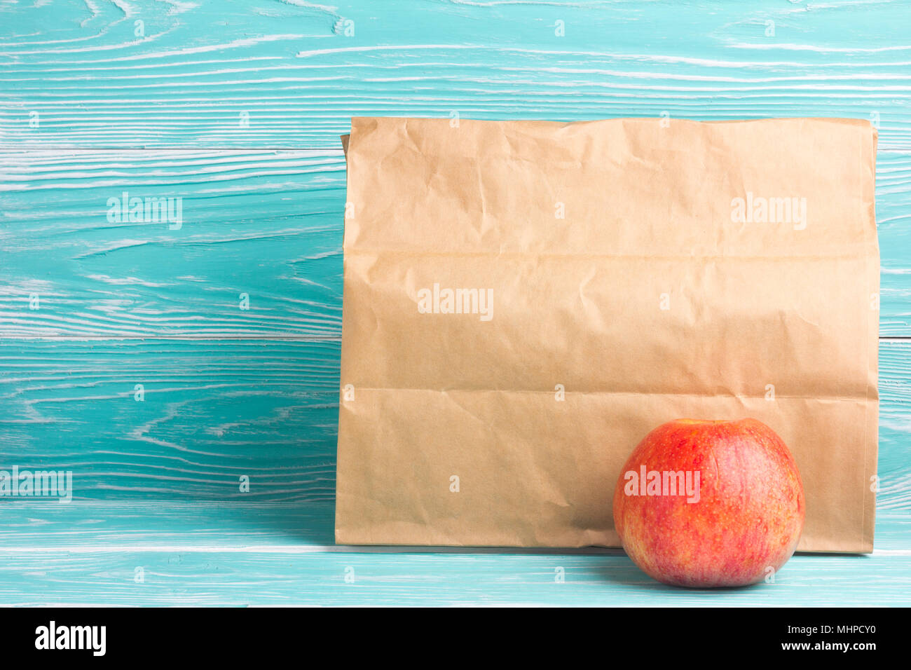 Leere Lunch Bag mit Apple auf Blau Holz- Hintergrund Stockfoto