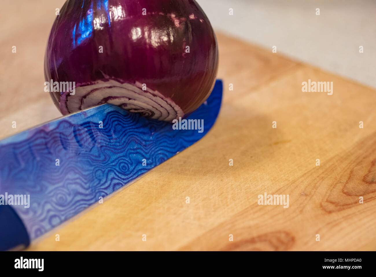 Rote Zwiebel auf einem blauen Messer über eine Holz Schneidebrett. Stockfoto