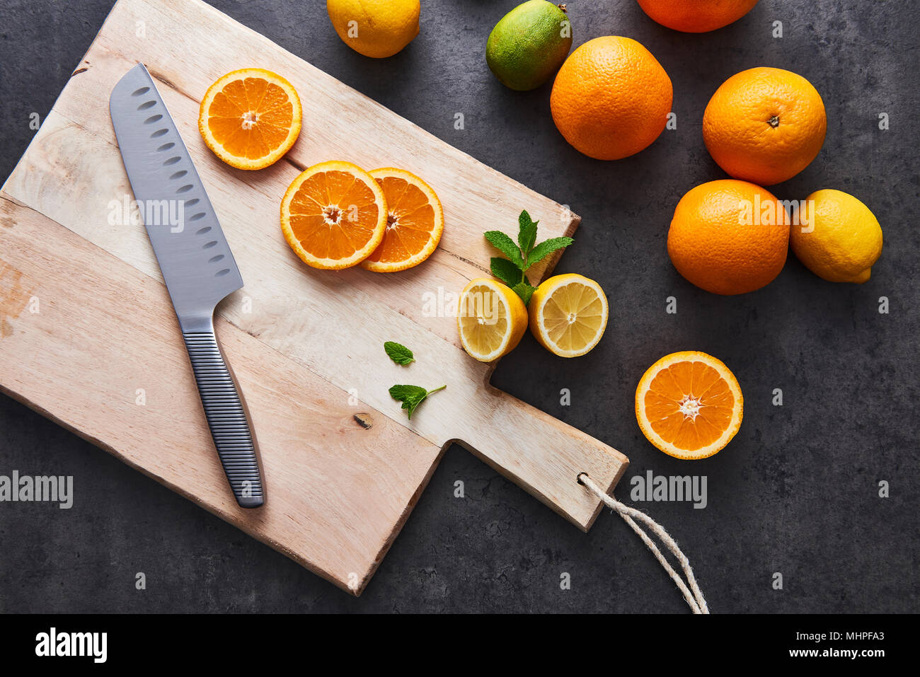 Flach von frischen Zitrusfrüchten, halb Orange und Zitronen auf Schneidebrett mit Messer an schwarzen Stein Hintergrund. Horizontale Ansicht von oben. Stockfoto